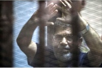 Egypt&#039;s deposed president Mohamed Morsi raises his hands from behind the defendant&#039;s cage as the judge reads out his verdict sentencing him and more than 100 other defendants to death at the police academy in Cairo on Saturday.